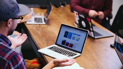 Mann mit Brille und Kappe sitzt am Tisch vor Laptop