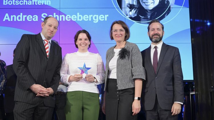 Zwei Frauen und zwei Männer stehen auf einer Bühne, eine Frau hält einen Pokal in der Hand