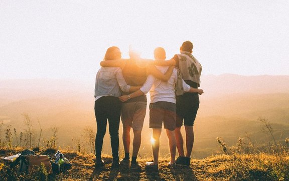 Vier junge Menschen von hinten zu sehen blicken in den Sonnenuntergang