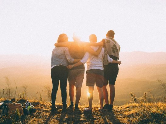 Vier junge Menschen von hinten zu sehen blicken in den Sonnenuntergang