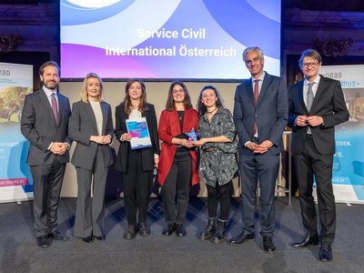 Gruppenbild Männer und Frauen in festlicher Kleidung. Vier Frauen in der Mitte des Bildes, eine davon hält einen Stern in der Hand, eine eine Urkunde 
