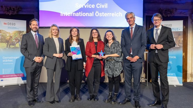 Gruppenbild Männer und Frauen in festlicher Kleidung. Vier Frauen in der Mitte des Bildes, eine davon hält einen Stern in der Hand, eine eine Urkunde 
