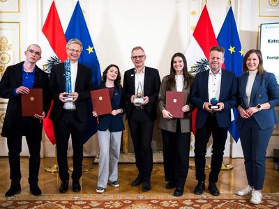 Gruppenfoto mit sieben Personen, alle in festlicher Kleidung, siehe halten Urkunden oder Pokale in den Händen