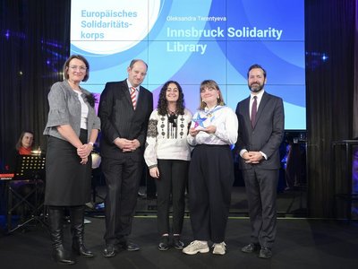 Europa bewegt: Erasmus+ und ESK Award 2024 Gruppenfoto von drei Frauen und zwei Männern auf einer Bühne, dahinter ein Screen mit dem Schriftzug „Innsbruck Solidarity Library“