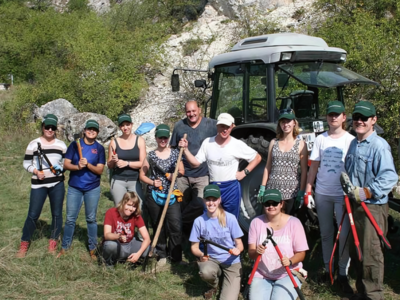 Eine Gruppe junger Menschen steht mit Landmaschinengeräten für einem Traktor und lacht in die Kamera