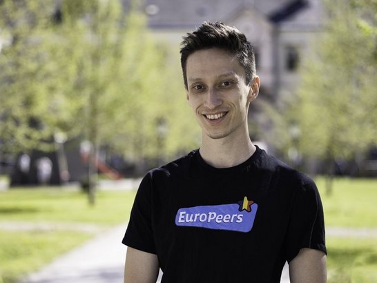 Junger Mann mit dunklen Haare lacht in die Kamera